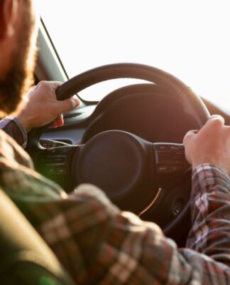 A imagem mostra um homem de costas dirigindo com uma camisa xadrez e as duas mãos no volante