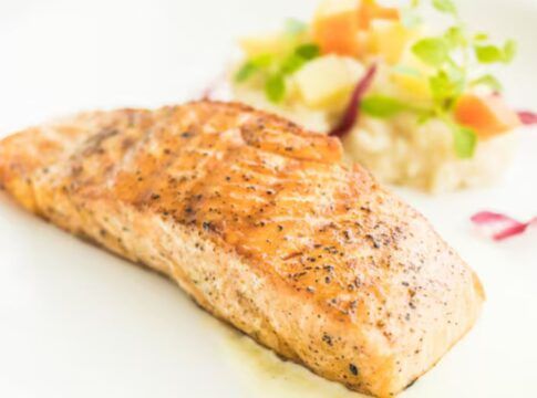 Pedaço de peixe em um prato branco com porção de vinagrete