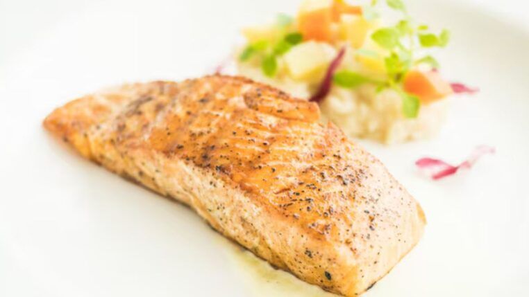 Pedaço de peixe em um prato branco com porção de vinagrete