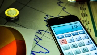 Foto de um celular, com o aplicativo da calculadora aberta, em cima de uma folha com um gráfico genérico