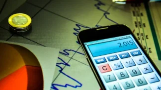 Foto de um celular, com o aplicativo da calculadora aberta, em cima de uma folha com um gráfico genérico