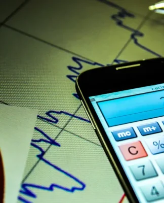 Foto de um celular, com o aplicativo da calculadora aberta, em cima de uma folha com um gráfico genérico