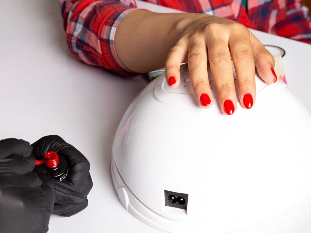 Mãos com as unhas pintadas com esmalte vermelho em cima de cabine