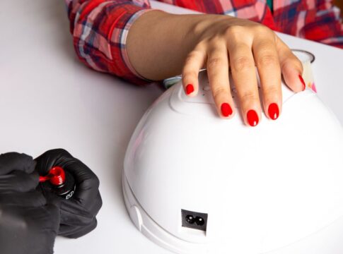 Mãos com as unhas pintadas com esmalte vermelho em cima de cabine