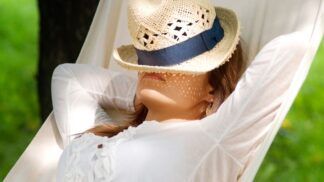 Mulher descansando em momento de lazer com chapéu no rosto e deitada na rede