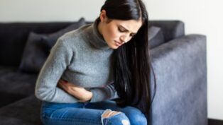 Mulher sentada no sofá com dor de barriga