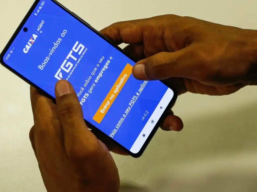 A imagem mostra as mãos de uma pessoa segurando o celular. Na tela do aparelho está o aplicativo do FGTS