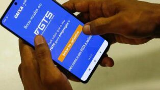 A imagem mostra as mãos de uma pessoa segurando o celular. Na tela do aparelho está o aplicativo do FGTS