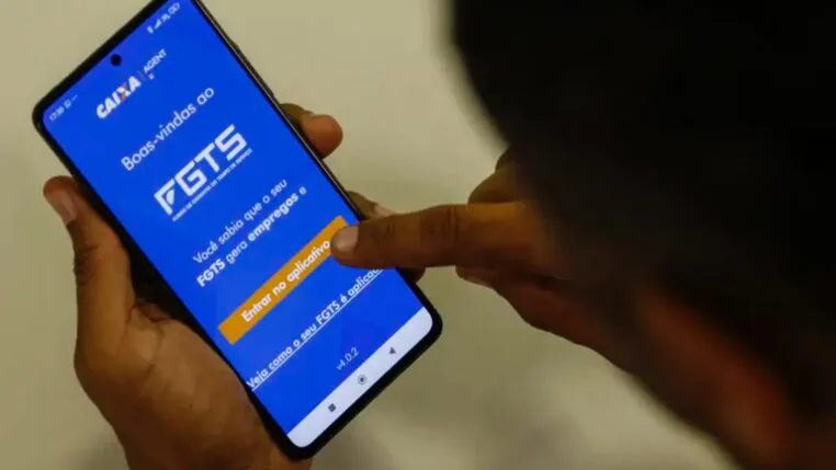 Imagem mostra homem segurando o celular e na tela do aparelho está o aplicativo do FGTS
