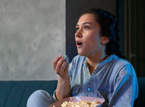 Imagem colorida de mulher comendo pipoca e assistindo filme