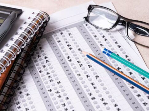 Página de prova com questões assinaladas. Lápis e óculos encima