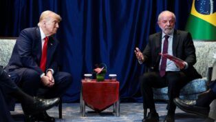 Uma foto em plano médio, que captura o momento de uma reunião formal, mostrando Donald Trump e Luiz Inácio Lula da Silva sentados de frente um para o outro, separados por uma pequena mesa.