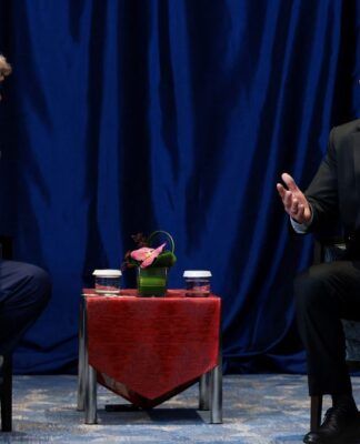 Uma foto em plano médio, que captura o momento de uma reunião formal, mostrando Donald Trump e Luiz Inácio Lula da Silva sentados de frente um para o outro, separados por uma pequena mesa.