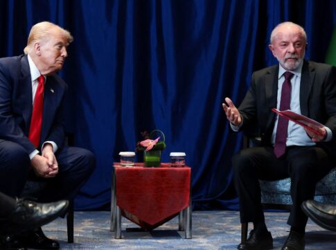 Uma foto em plano médio, que captura o momento de uma reunião formal, mostrando Donald Trump e Luiz Inácio Lula da Silva sentados de frente um para o outro, separados por uma pequena mesa.