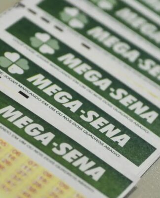 A imagem é um plano aproximado, em ângulo diagonal, que mostra vários bilhetes de apostas da loteria Mega-Sena. Os bilhetes estão empilhados ou dispostos lado a lado. Em primeiro plano, no canto inferior esquerdo, é possível ver as primeiras linhas da grade de números da aposta, impressas em tinta amarela e vermelha sobre o papel branco.