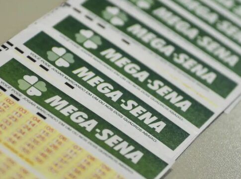 A imagem é um plano aproximado, em ângulo diagonal, que mostra vários bilhetes de apostas da loteria Mega-Sena. Os bilhetes estão empilhados ou dispostos lado a lado. Em primeiro plano, no canto inferior esquerdo, é possível ver as primeiras linhas da grade de números da aposta, impressas em tinta amarela e vermelha sobre o papel branco.