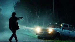 Homem apontando arma para um carro durante a noite