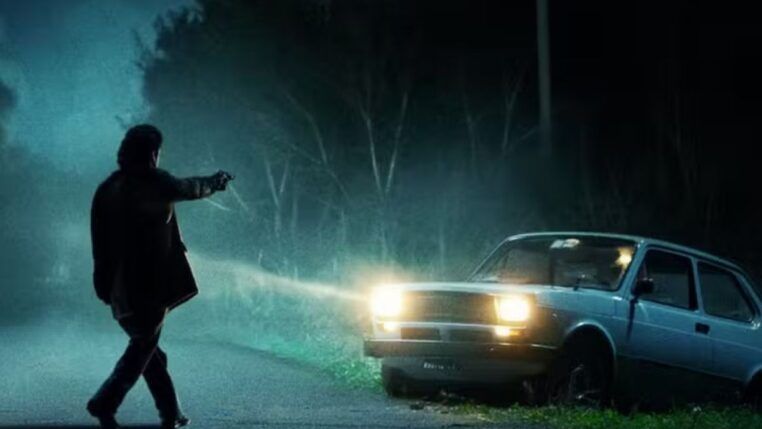 Homem apontando arma para um carro durante a noite