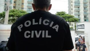 Imagem de um policial de costas com uma camisa preta. Na vestimenta, está escrito "Polícia Civil".
