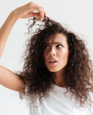 Mulher de cabelo cacheado com rosto de assustada segurando a mecha do cabelo