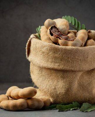 Diversos frutos de tamarindo em um saco de tecido. O fundo é preto.
