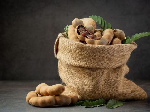Diversos frutos de tamarindo em um saco de tecido. O fundo é preto.