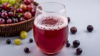 Copo de suco de uva, com várias uvas roxas no fundo