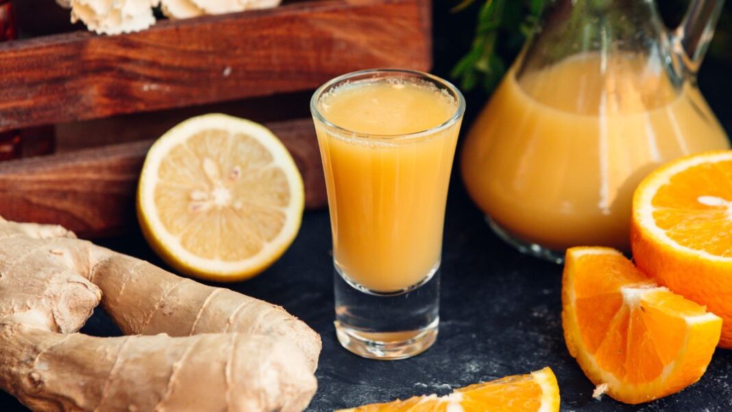 Copo suco de larnaja com laranja e gengibres ao redor