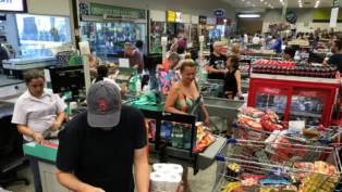 Pessoas em fila de supermercado, com compras.