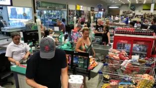 Pessoas em fila de supermercado, com compras.