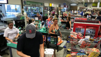 Pessoas em fila de supermercado, com compras.