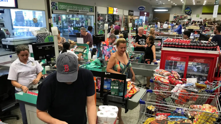 Pessoas em fila de supermercado, com compras.