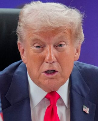 Um close-up (plano fechado) de Donald Trump, sentado em uma cadeira de encosto alto (provavelmente em uma reunião), olhando diretamente para a câmera.