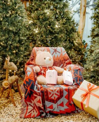 Poltrona com urso de pelúcia e várias árvores natalinas em volta.