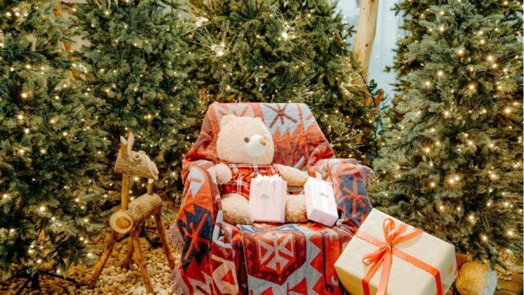 Poltrona com urso de pelúcia e várias árvores natalinas em volta.