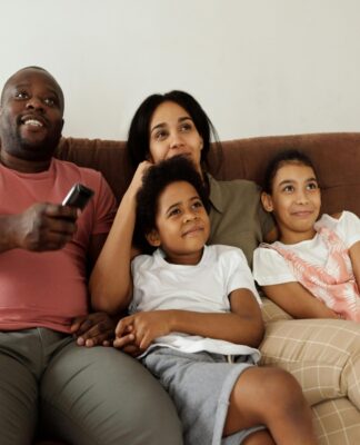 Uma família sentada no sofá assistindo um filme. Um homem está com controle na mão