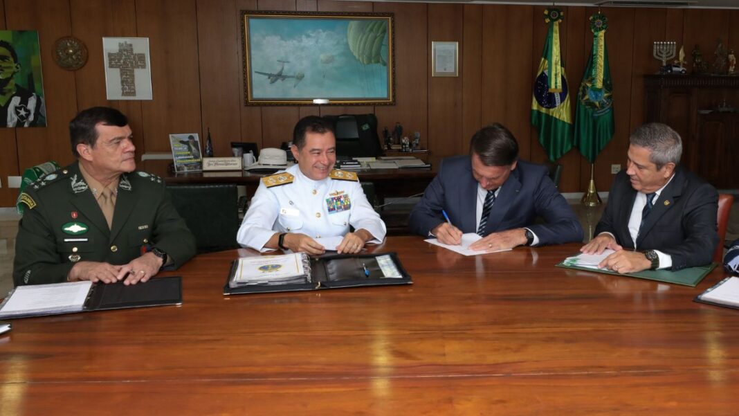 Esta é uma foto em plano médio, tirada em um ambiente de escritório ou gabinete presidencial, mostrando o ex-presidente Jair Bolsonaro sentado a uma mesa com três figuras militares.