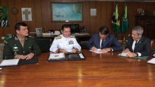 Esta é uma foto em plano médio, tirada em um ambiente de escritório ou gabinete presidencial, mostrando o ex-presidente Jair Bolsonaro sentado a uma mesa com três figuras militares.