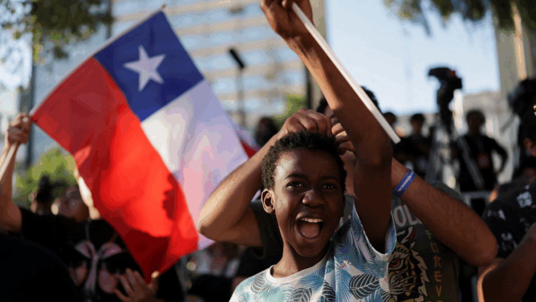 Garoto em manifestação, com bandeira do Chile ao fundo