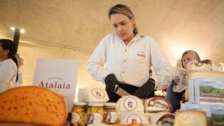 Mulher corta queijo diante de diversas peças