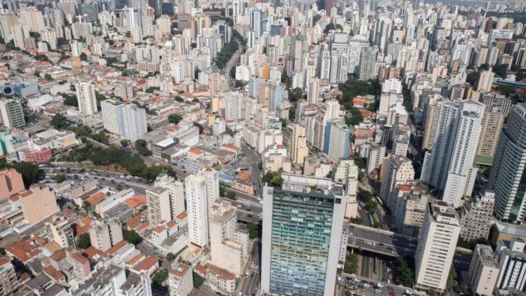 Do alto aparecem casas e diversos prédios da zona central de São Paulo