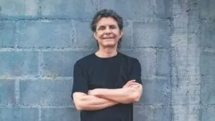 Lô Borges encostado em uma parede de tijolos cinza