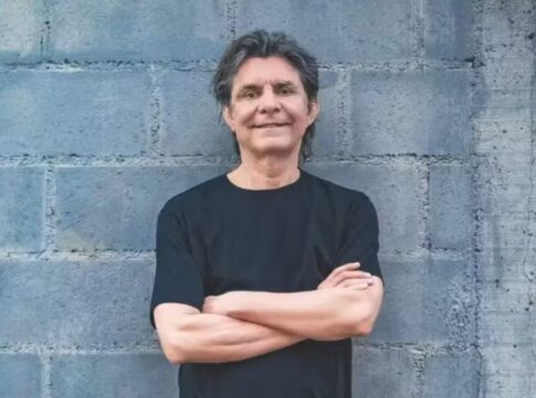 Lô Borges encostado em uma parede de tijolos cinza