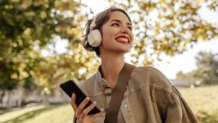 Garota com fone feliz andando em um parque.