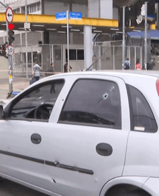 imagem de veículo com marcas de tiros parado no meio de uma avenida