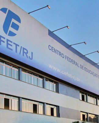 Fachada do prédio do CEFET/RJ, com placas institucionais visíveis, janelas amplas e bandeiras hasteadas, cercado por palmeiras e carros estacionados em frente.