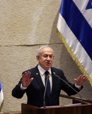 Primeiro-ministro de Israel, Benjamin Netanyahu, fala ao microfone à frente da bandeira do seu país