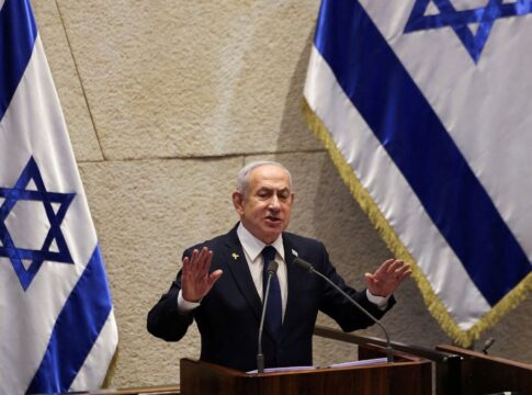 Primeiro-ministro de Israel, Benjamin Netanyahu, fala ao microfone à frente da bandeira do seu país