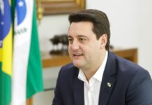 Ratinho Junior sentado em seu gabinete, com bandeira do Paraná ao fundo