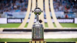 Taça da Libertadores no gramado, com símbolo da competição ao fundo
